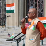 A person with the US and Indian flags talking with a microphone